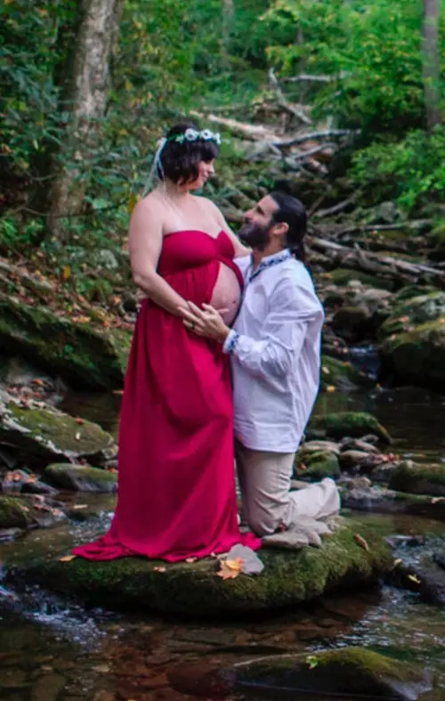 Photo of Phoenix Be kneeling beside a pregnant woman in a creek
